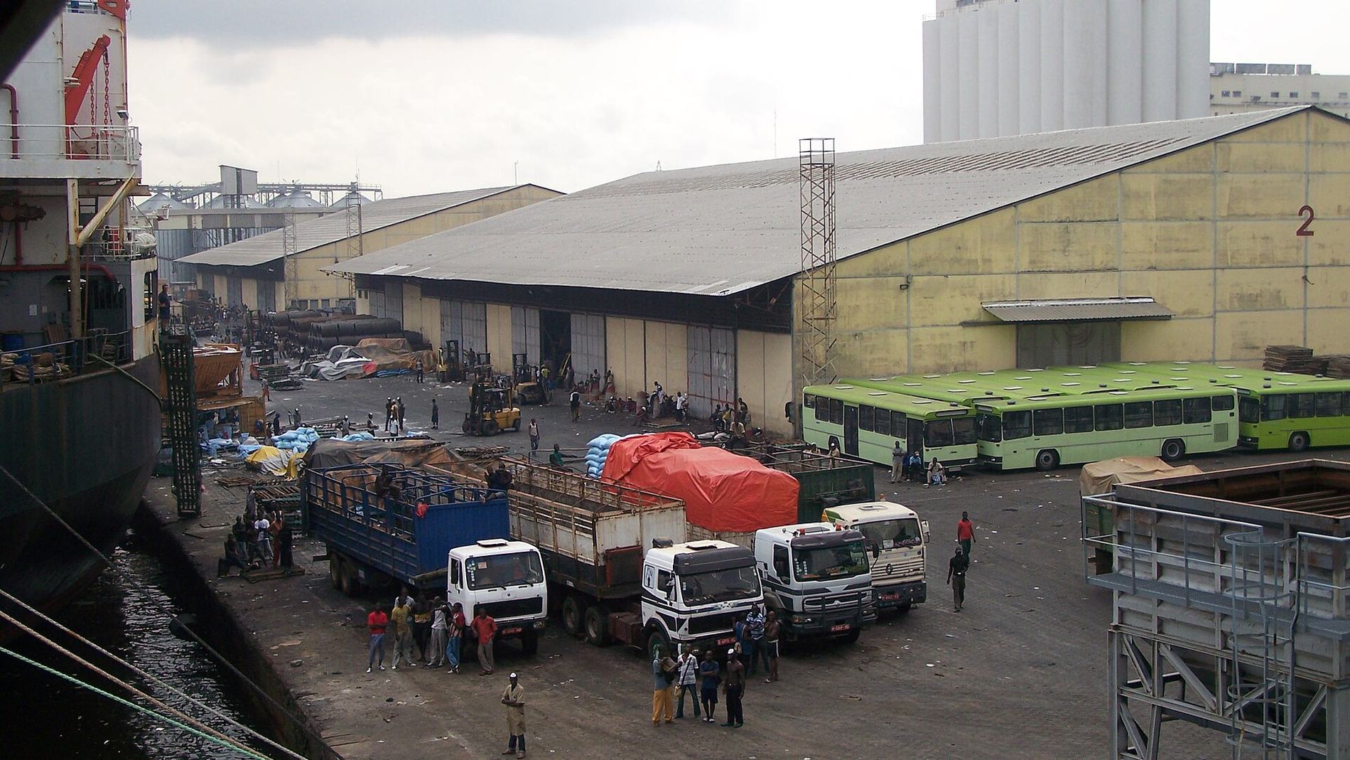 Trucks drawn up beside a port transit shed, cargo handled on the apron.