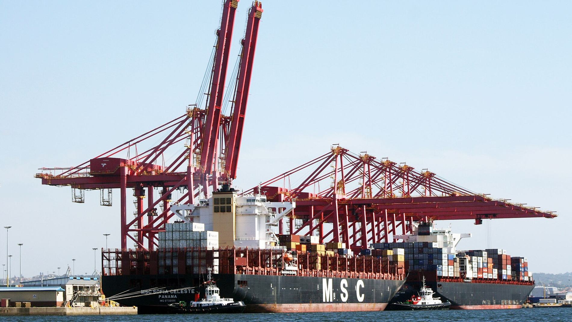A container ship alongside a terminal, gantry cranes working her.
